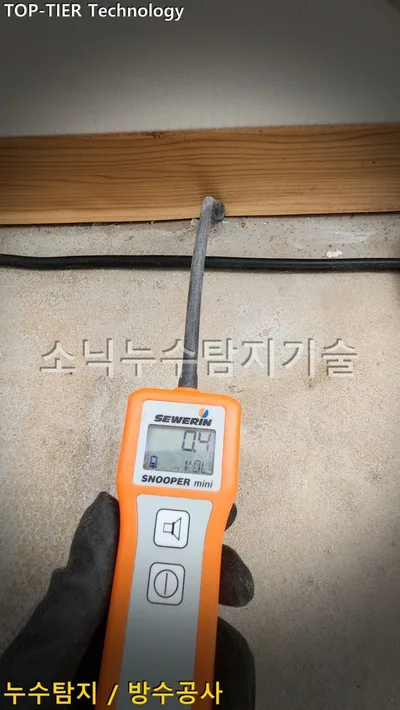 대구 달서구 호산동 누수, 벽 아래 나무 걸레받이와 바닥이 만나는 틈에 검출봉을 댄 주황색 휴대용 가스 검출기