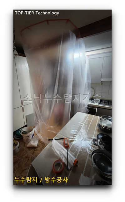 주방 작업 구간을 천장부터 바닥까지 반투명 비닐로 감싸 격리한 보양 작업 모습, 옆에 그릇과 공구가 놓여 있다