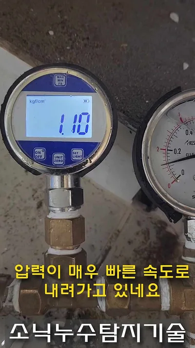 세면대 배관에 물린 파란 디지털 압력계가 1.10을 표시하고 옆에 아날로그 게이지가 함께 걸린 모습