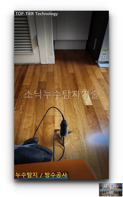 대구 수성구 신세계타운 누수, 나무 마루 바닥에 세운 청음 센서와 장갑 낀 손, 주황색 본체